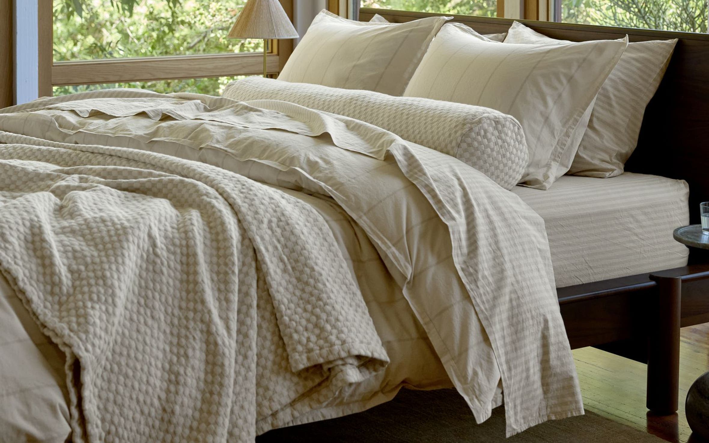 A beautifully made bed surrounded by windows and greenery.