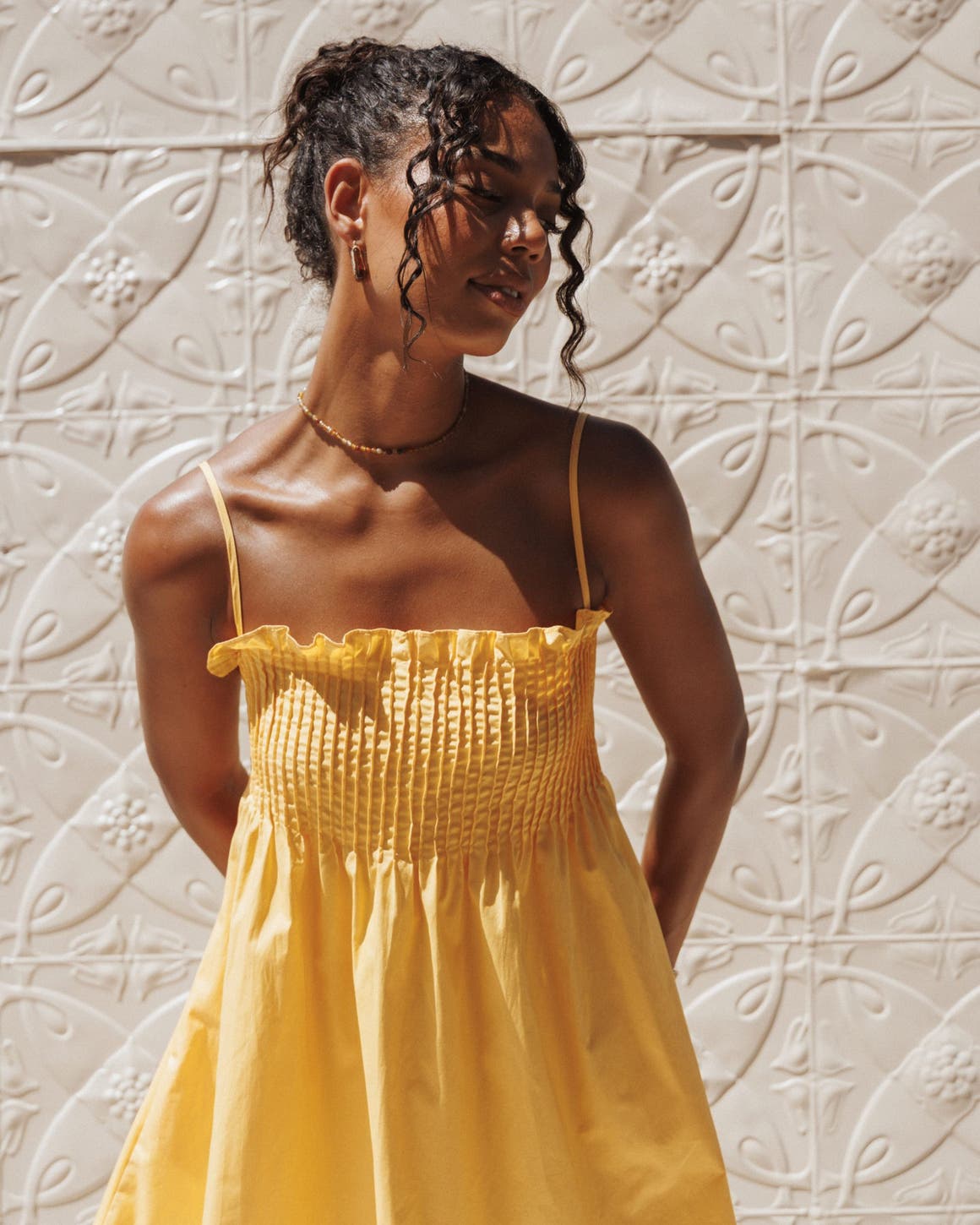 A woman wearing a bright yellow sundress with thin straps and a smocked bodice.