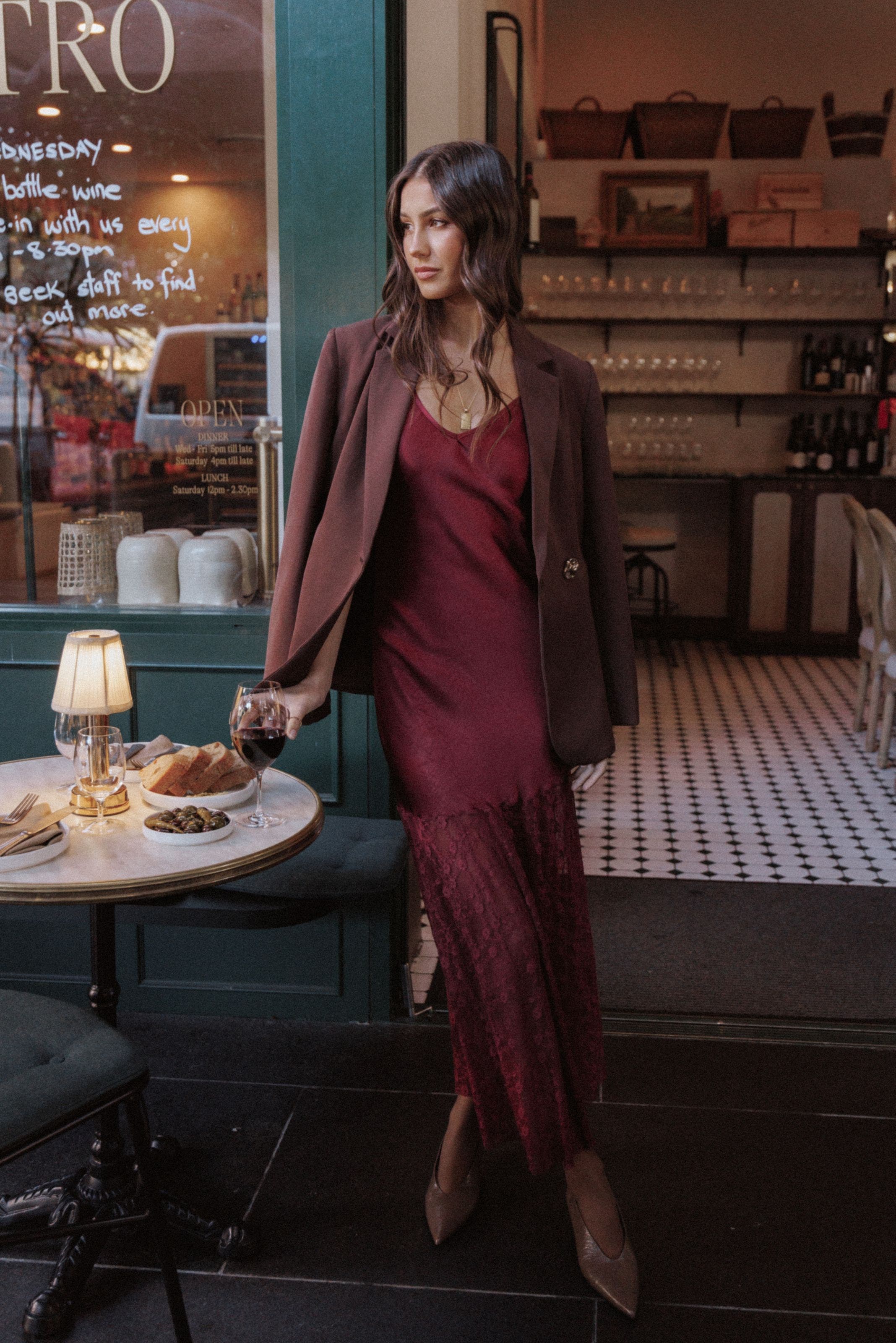 A woman wearing a burgundy lace-hem dress with a blazer and heels.