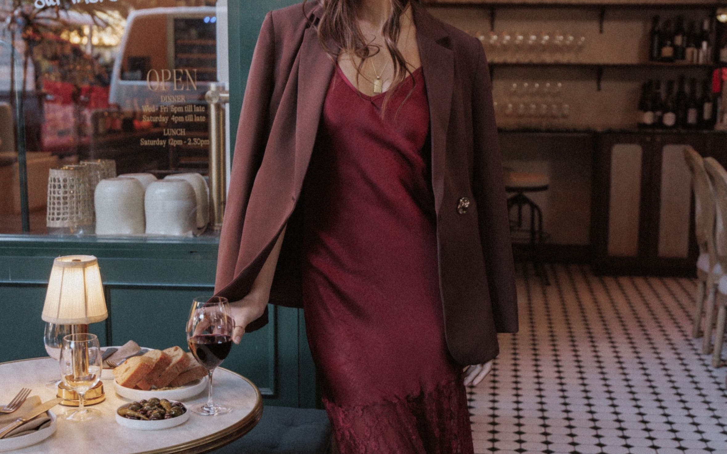 A woman wearing a burgundy lace-hem dress with a blazer and heels.