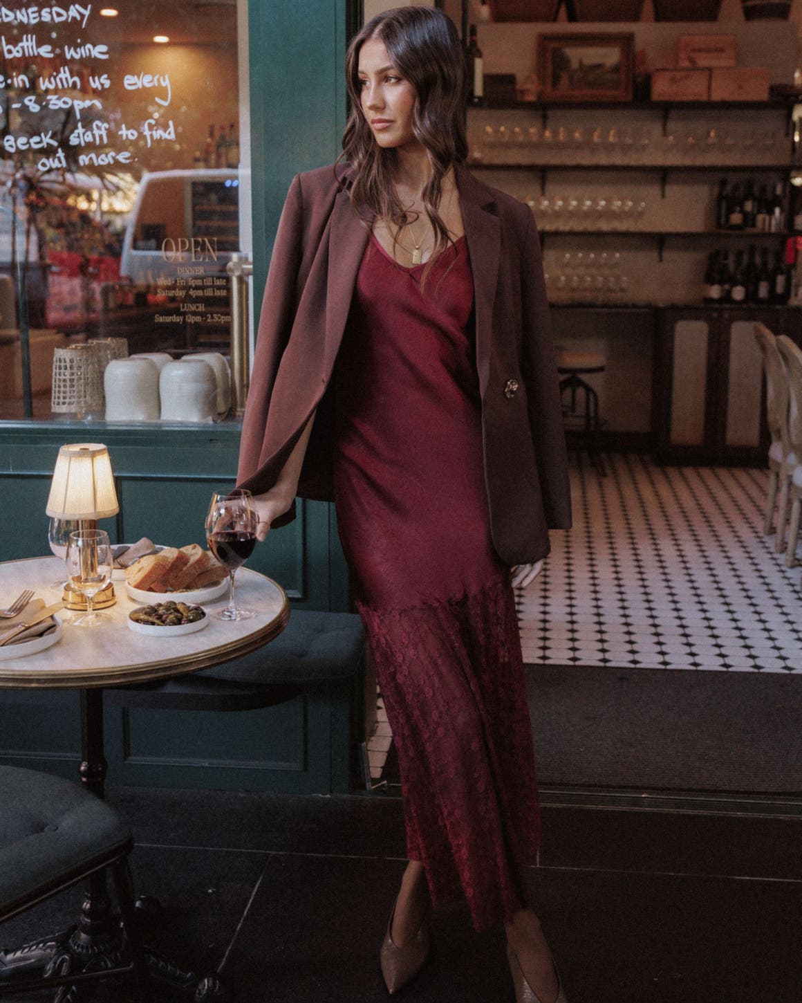 A woman wearing a burgundy lace-hem dress with a blazer and heels.