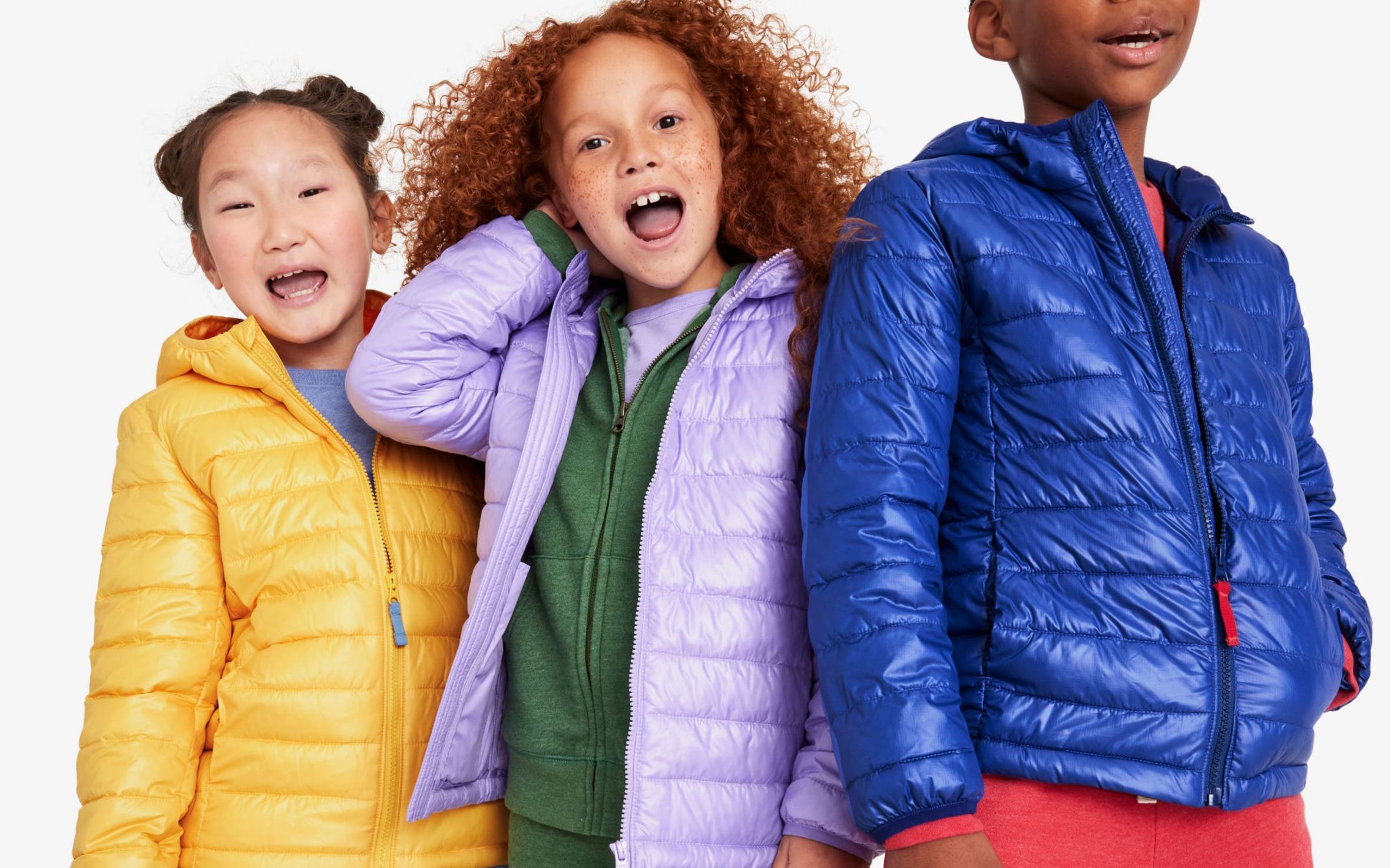 Three kids wearing bright winter coats and colorful sweats.