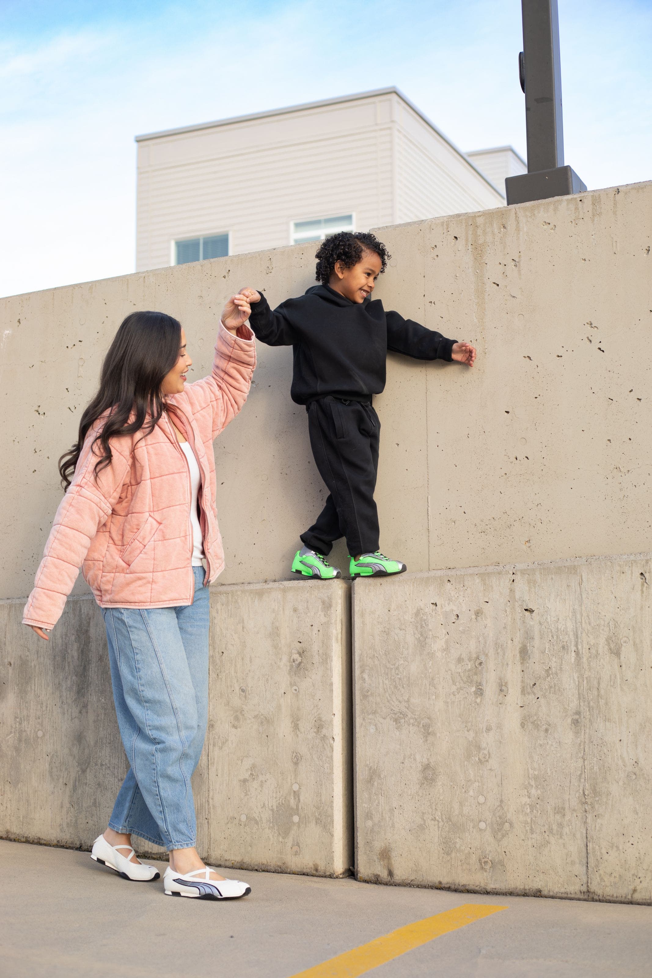Child wearing PUMA sneakers holding a woman's hand.