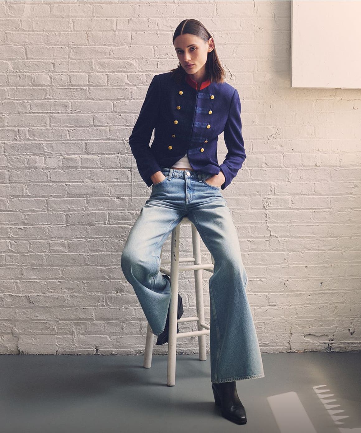 A woman sitting on a stool in a rag & bone jacket, jeans and boots. 