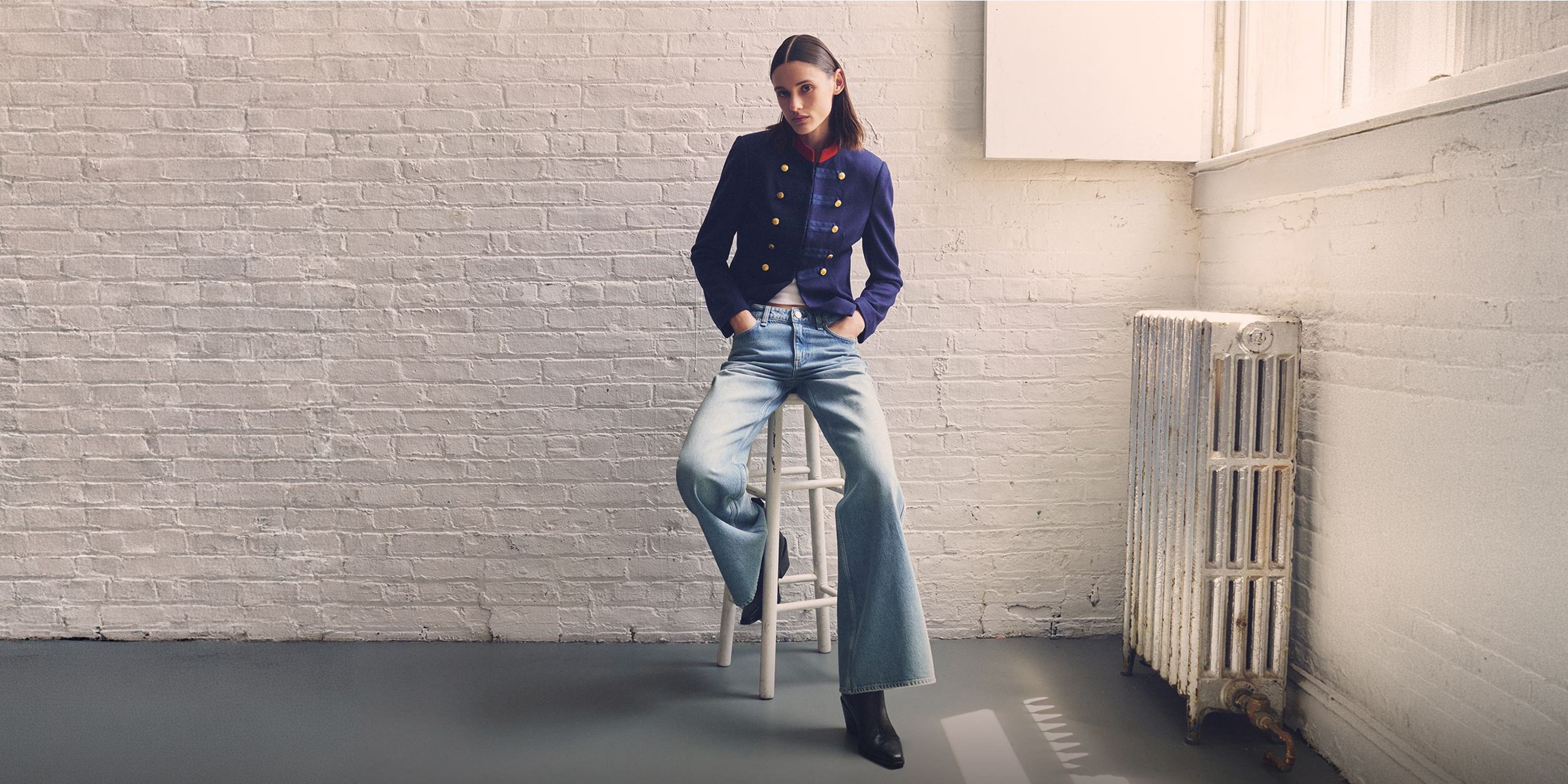 A woman sitting on a stool in a rag & bone jacket, jeans and boots. 