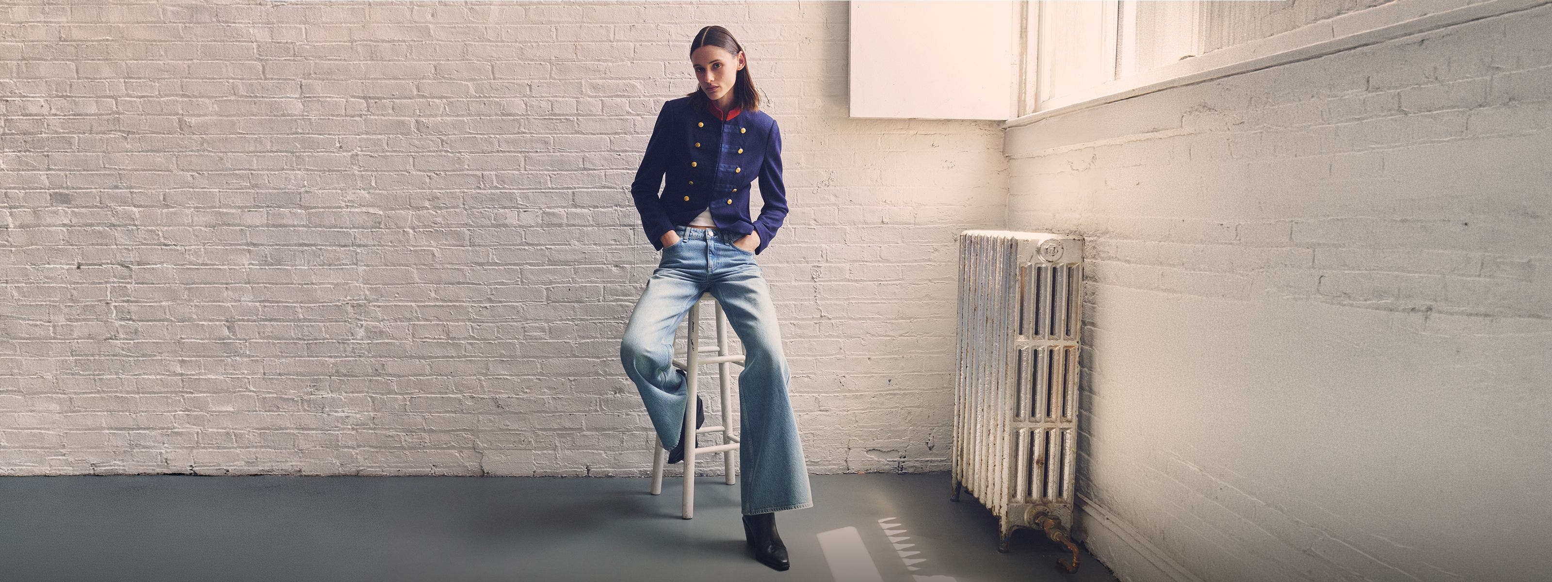 A woman sitting on a stool in a rag & bone jacket, jeans and boots. 
