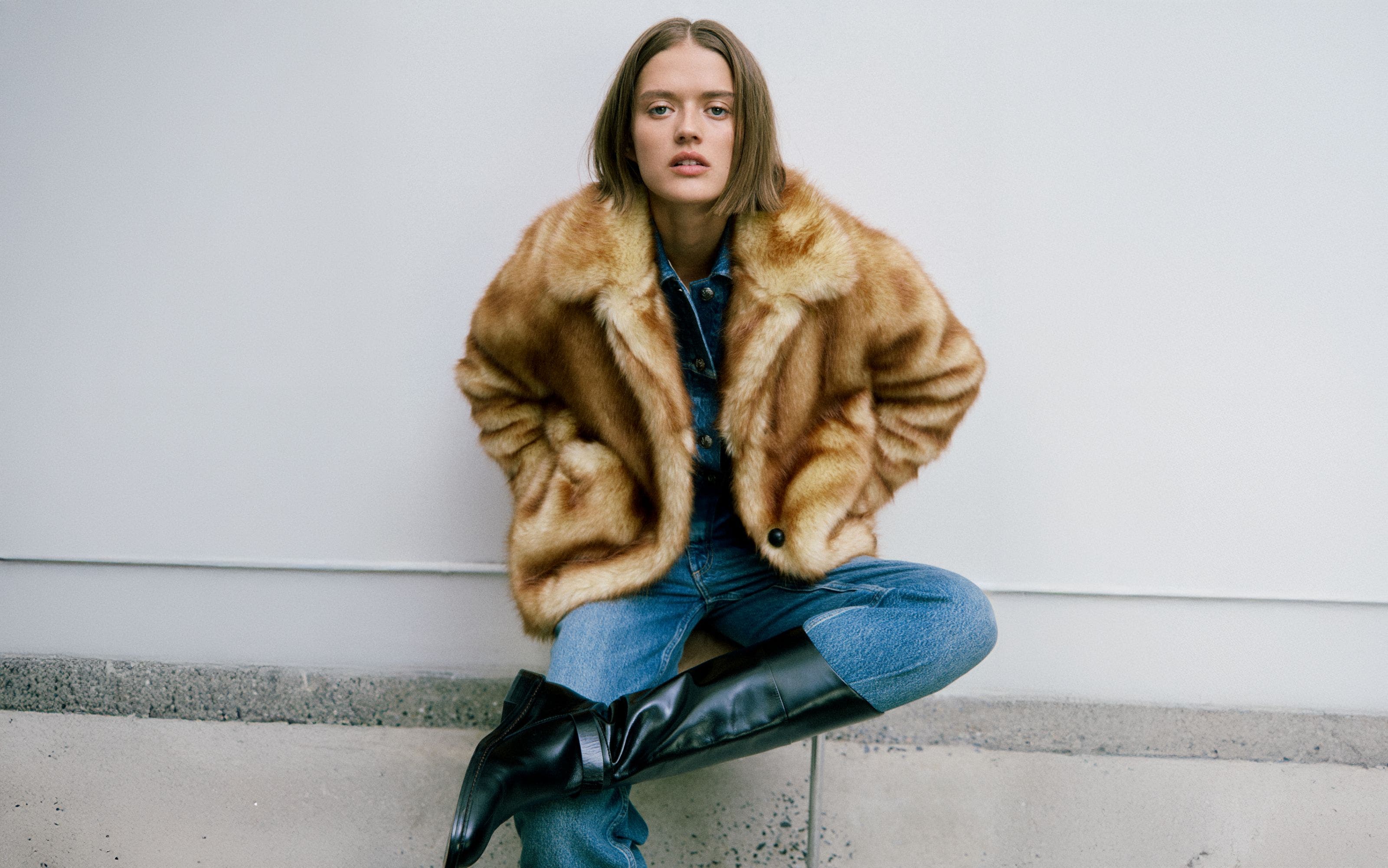 A woman wearing a faux-fur coat with jeans and knee-high boots.