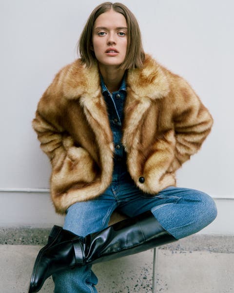 A woman wearing a faux-fur coat with jeans and knee-high boots.