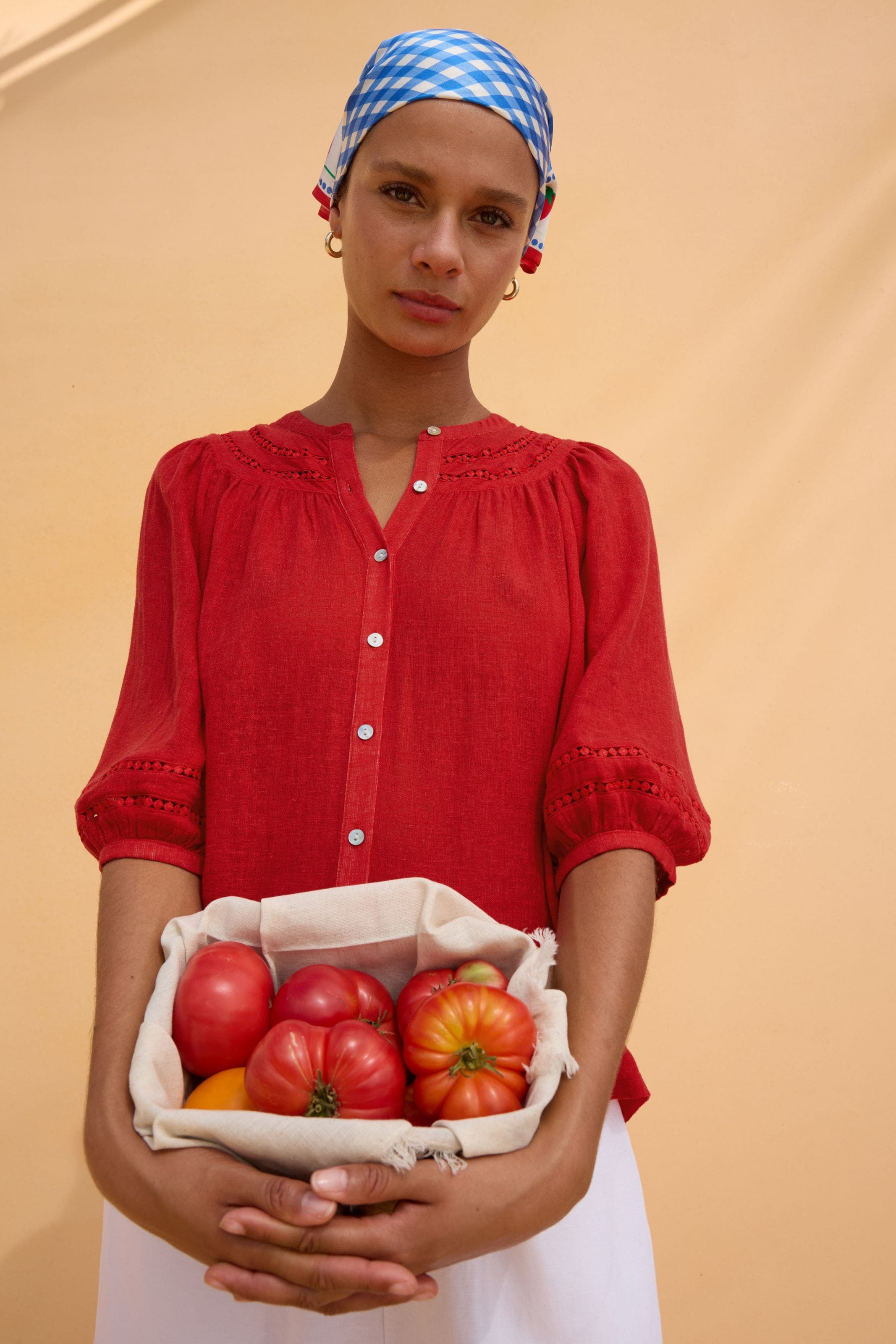 A woman wearing a gingham head scarf and red top carrying tomatoes.