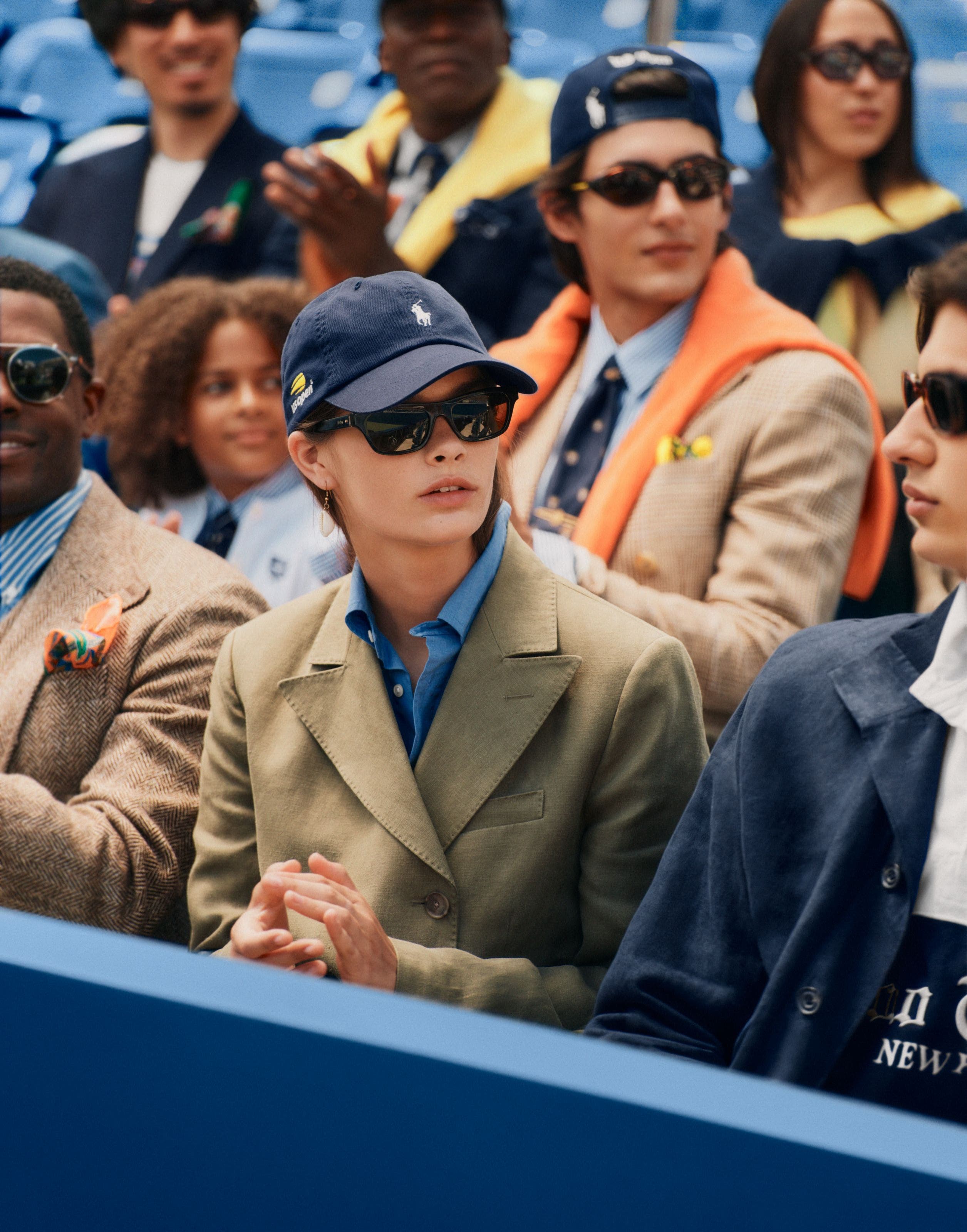 A woman in a crowd wearing a blazer, an Oxford shirt, and a baseball cap.