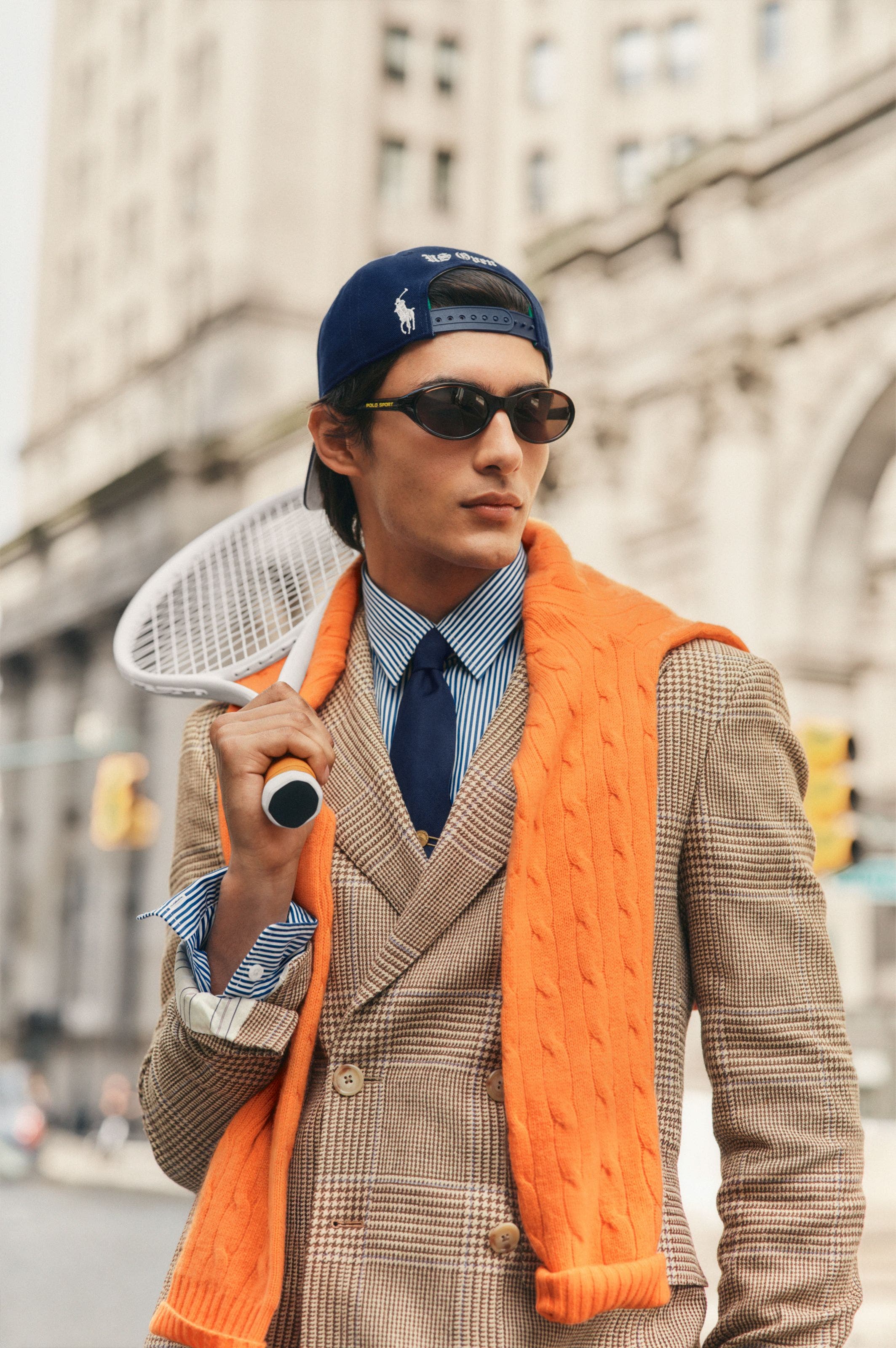 A man wearing a blazer over a button-up with a sweater on his shoulders.