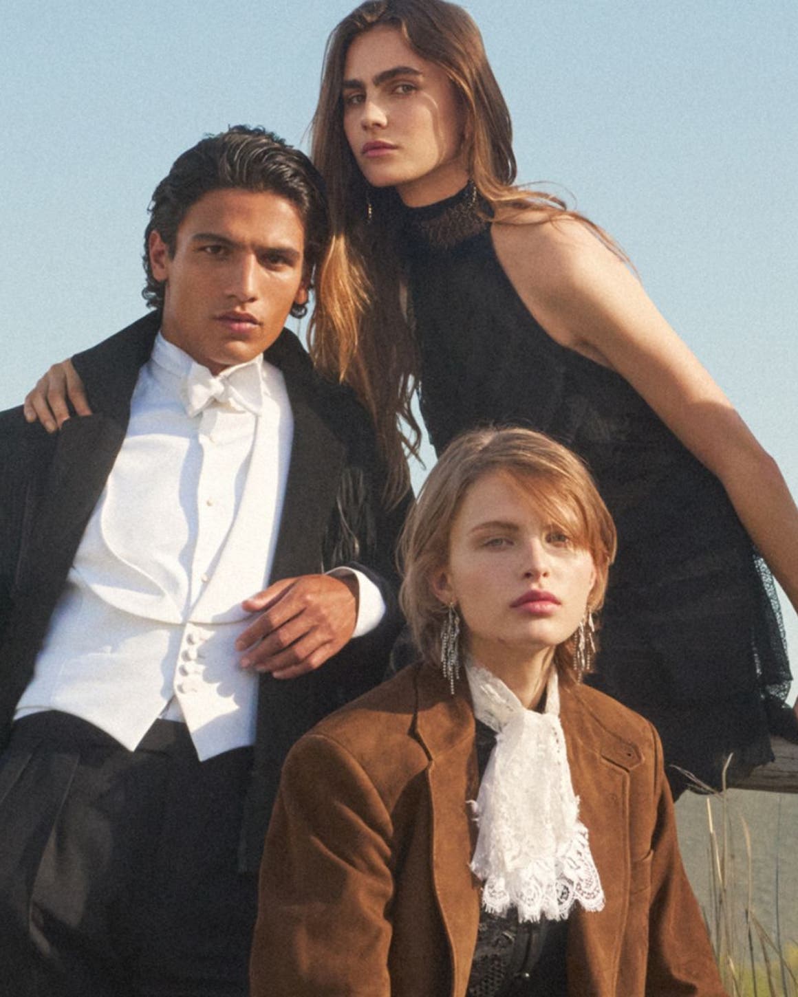 Seven models men and woman sitting on a ranch fence.