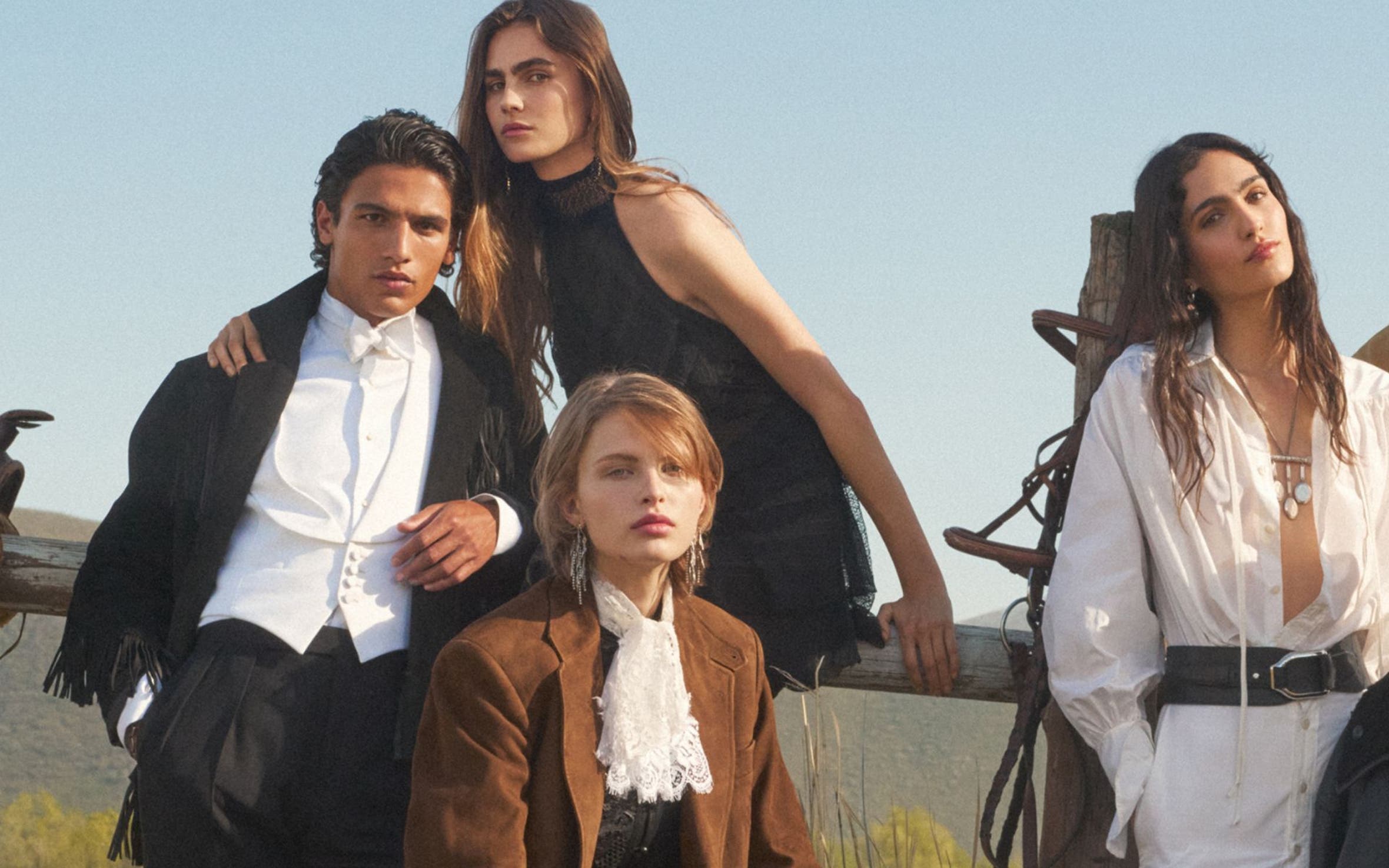 Seven models men and woman sitting on a ranch fence.