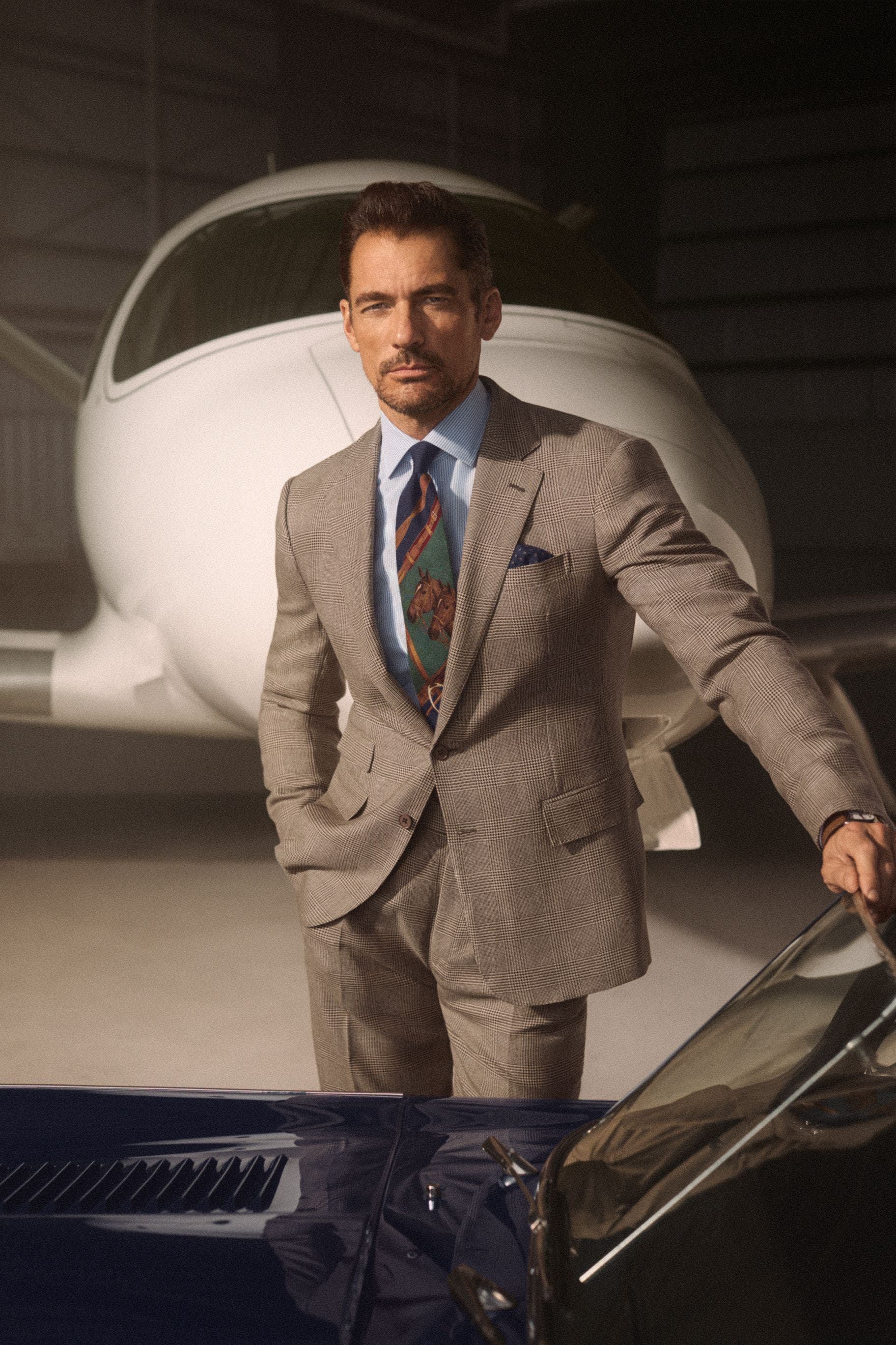 A man wearing a button-up shirt and equestrian-theme tie with a brown suit.