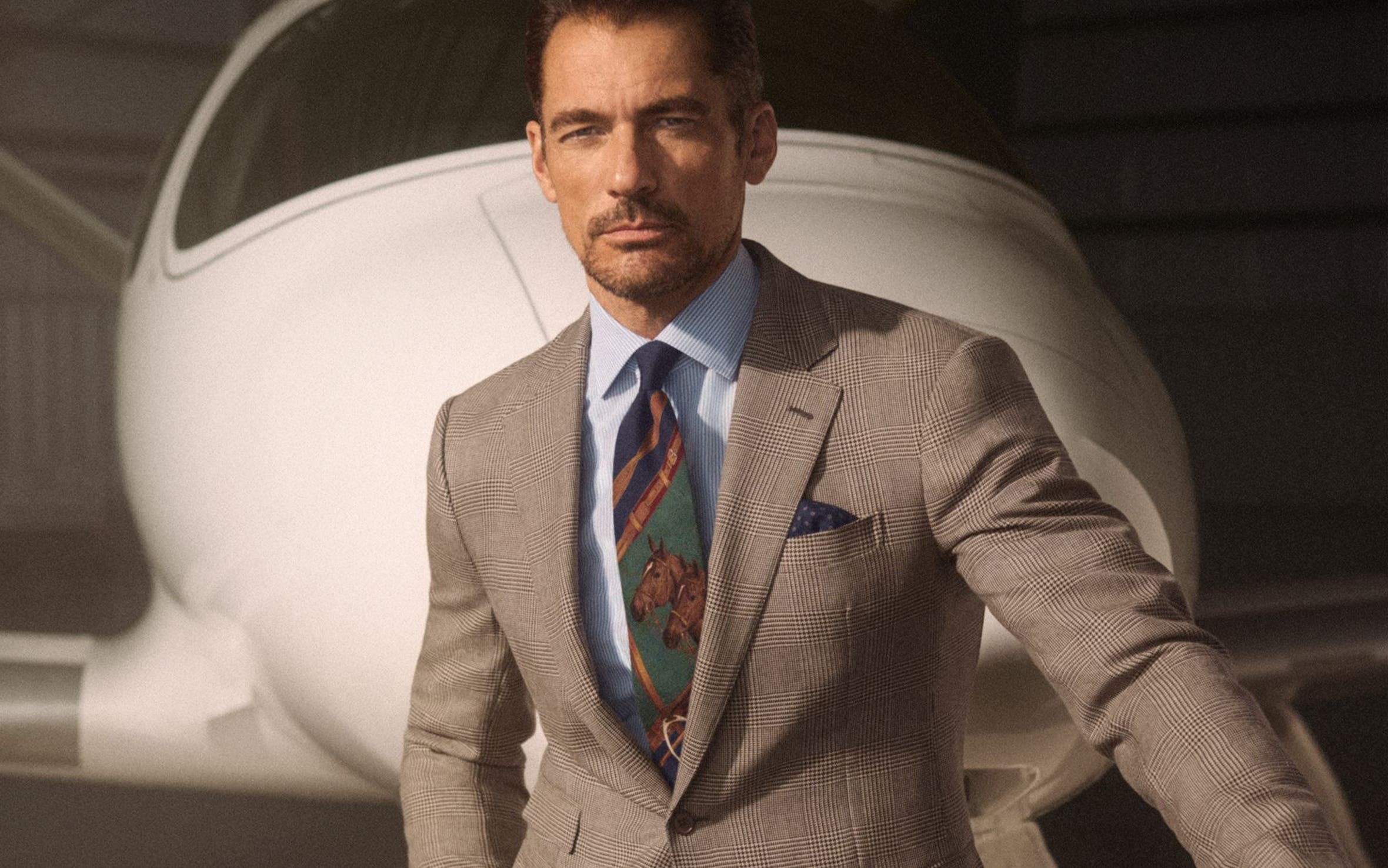 A man wearing a button-up shirt and equestrian-theme tie with a brown suit.