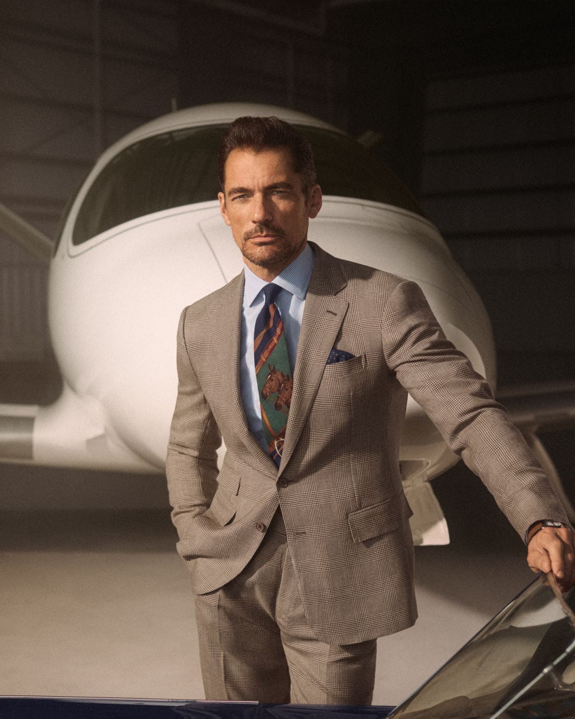 A man wearing a button-up shirt and equestrian-theme tie with a brown suit.