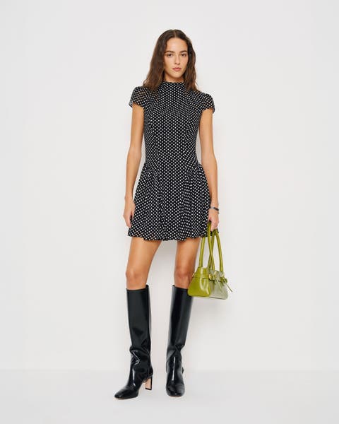 A woman wearing a polka dot minidress and knee-high boots.