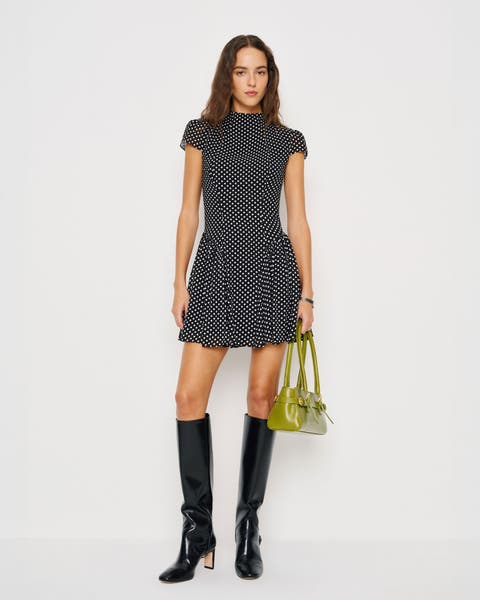 A woman wearing a polka dot minidress and knee-high boots.