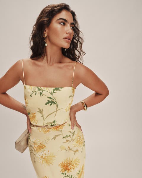 Woman wearing a pale yellow floral dress accented with a gold skinny belt from Reformation.