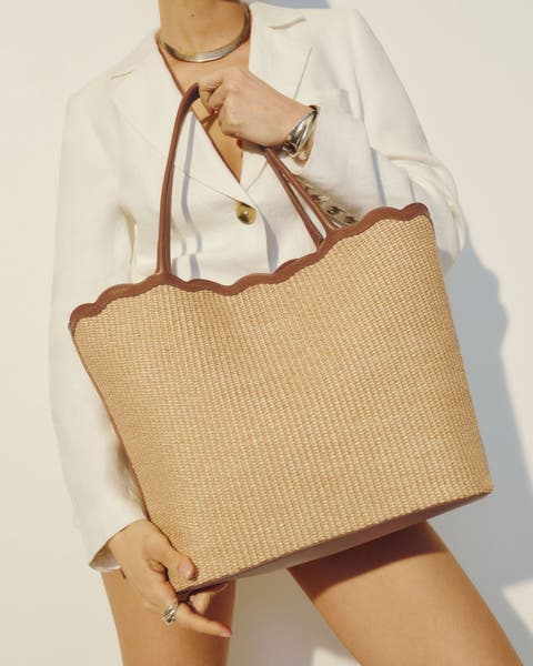 Woman holding a large straw tote with leather trim from Reformation.