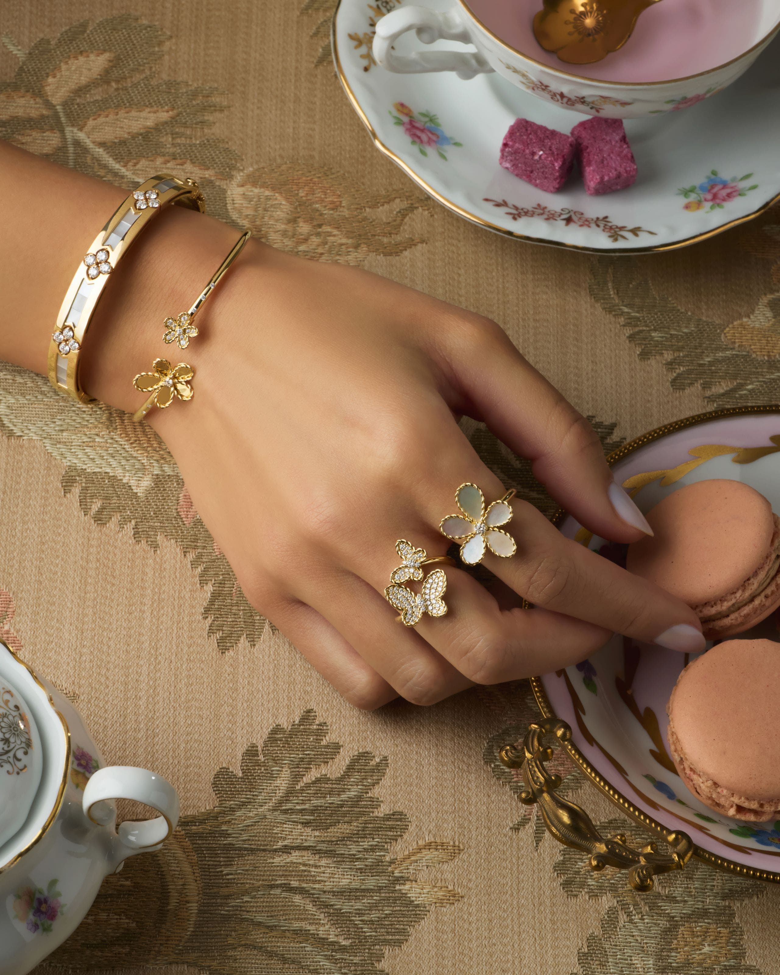 A pair of hands wearing intricate gold bracelets and rings. 