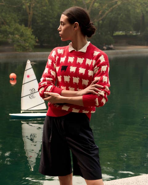 A woman wearing a red sweater embroidered with sheep and a pair of tailored shorts.