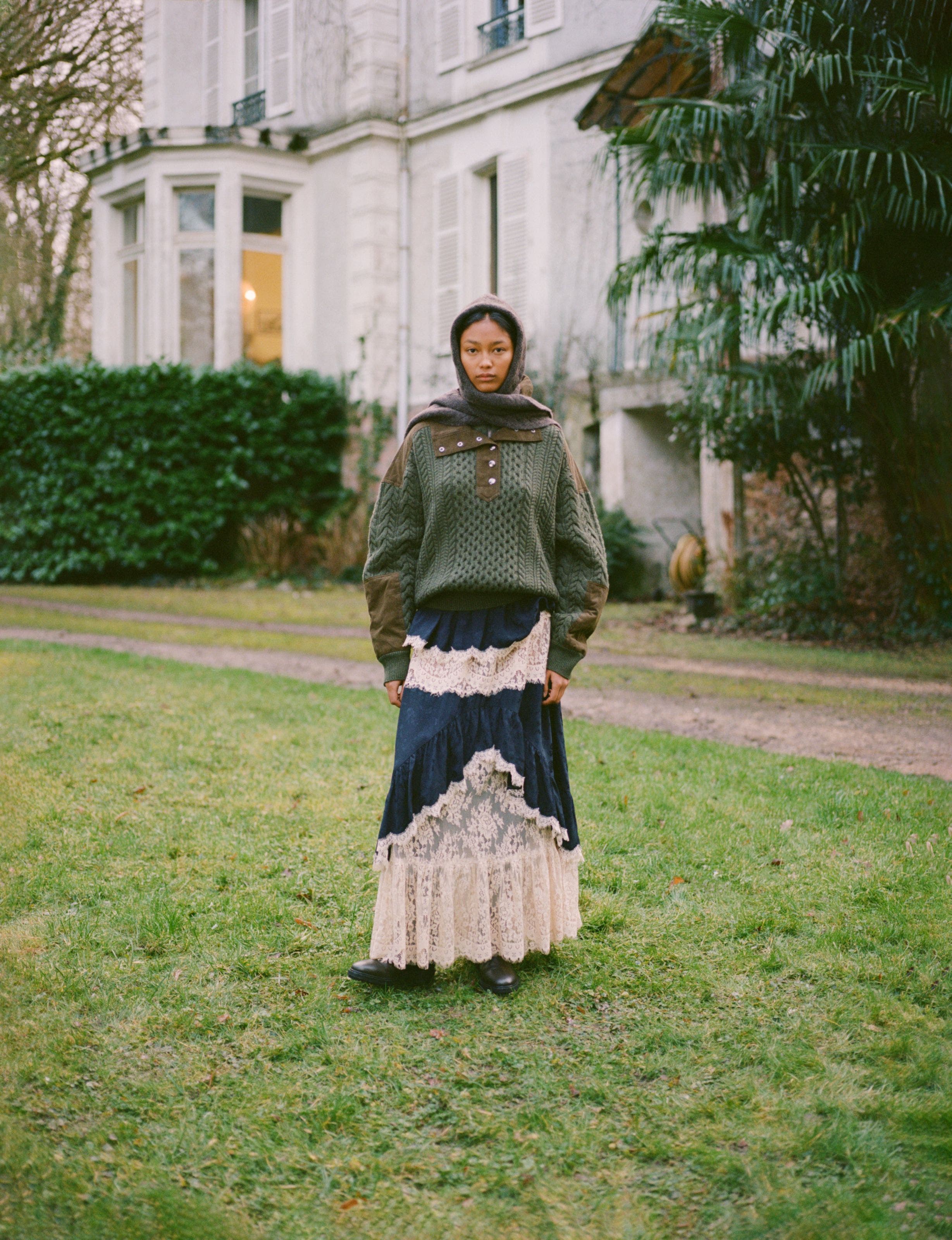 A woman wearing a forest green sweater over a blue lace dress.