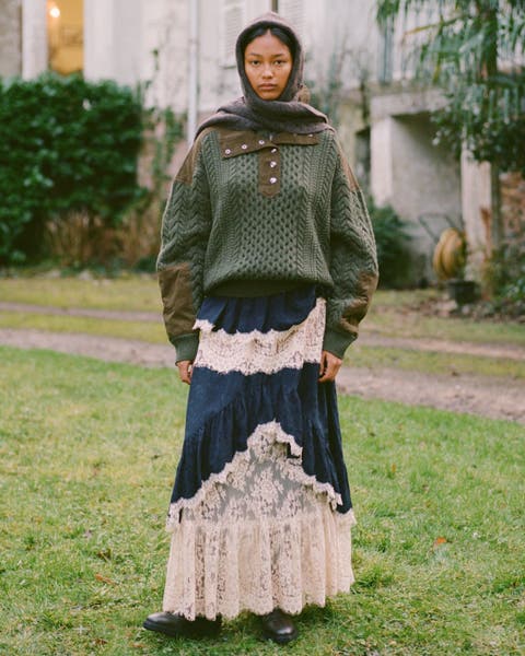 A woman wearing a forest green sweater over a blue lace dress.