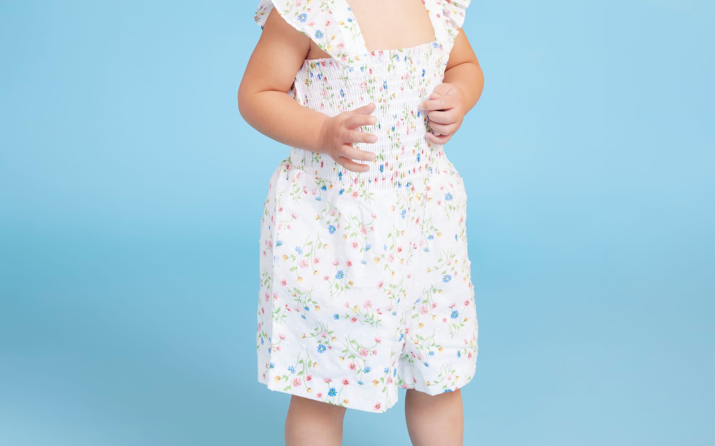 A toddler girl in pink sneakers and a floral romper.