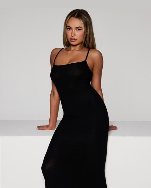 Woman wearing black form-fitting, spaghetti-strap dress by SKIMS.