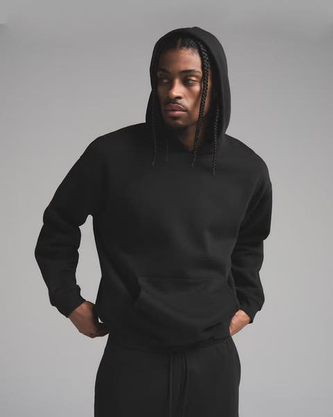 Man wearing black matching hooded sweatshirt and sweatpants by SKIMS.