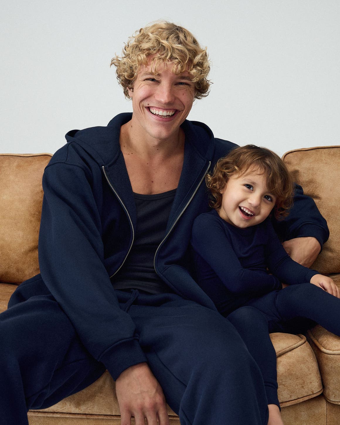 Man and his kid wearing matching navy SKIMS hoodies and sweatpants.