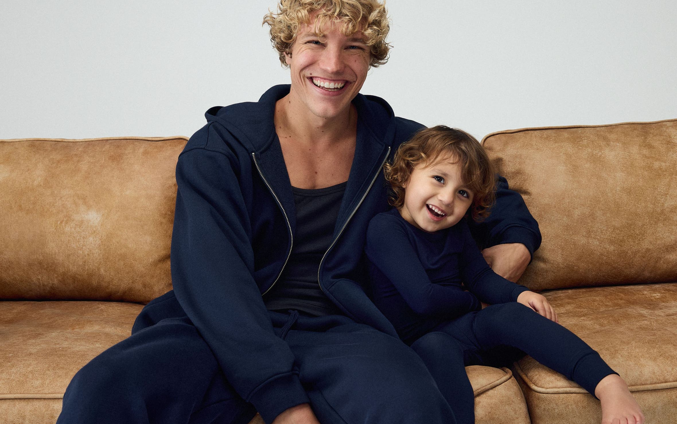 Man and his kid wearing matching navy SKIMS hoodies and sweatpants.