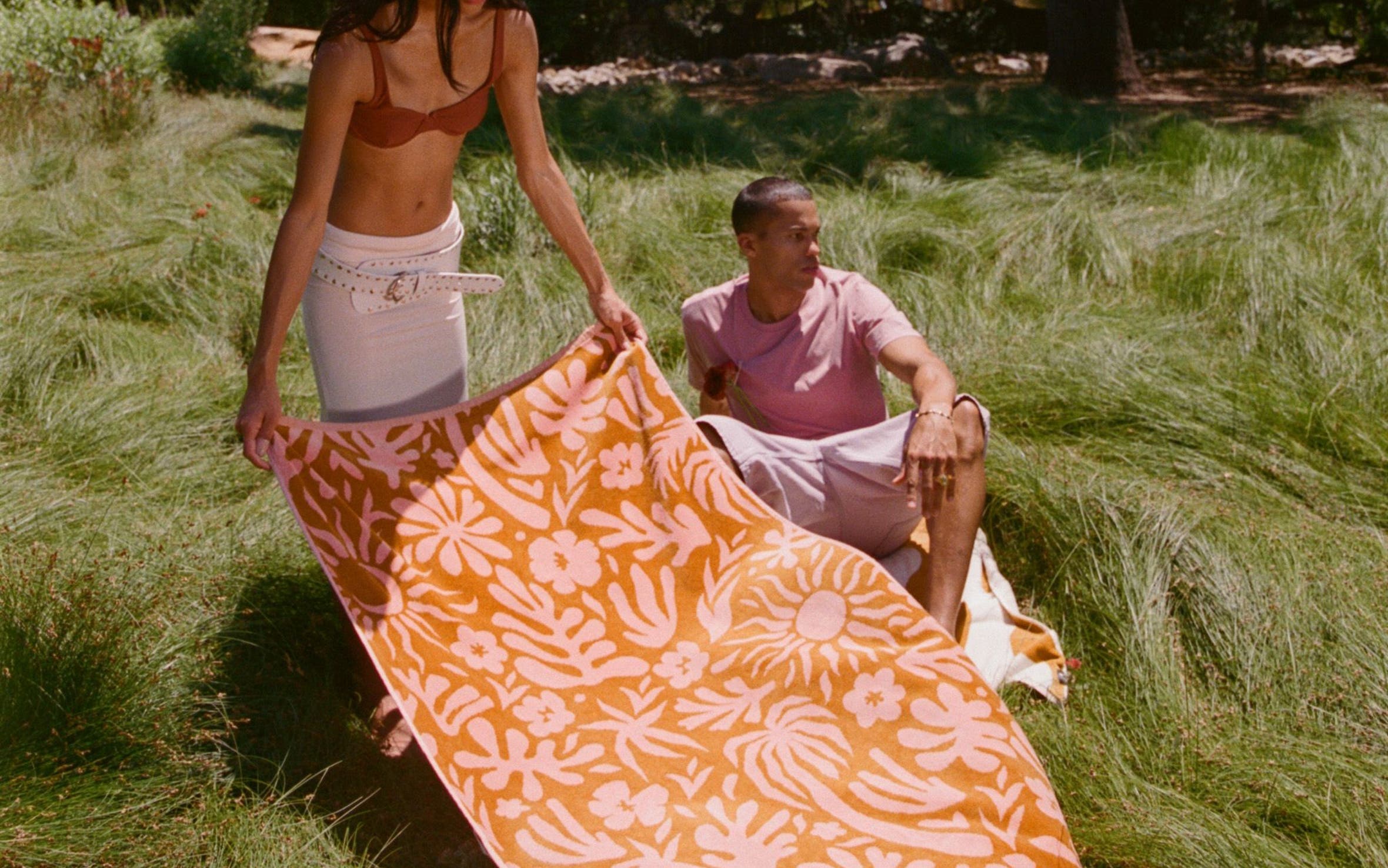 A woman spreading a patterned blanket on a grassy field.
