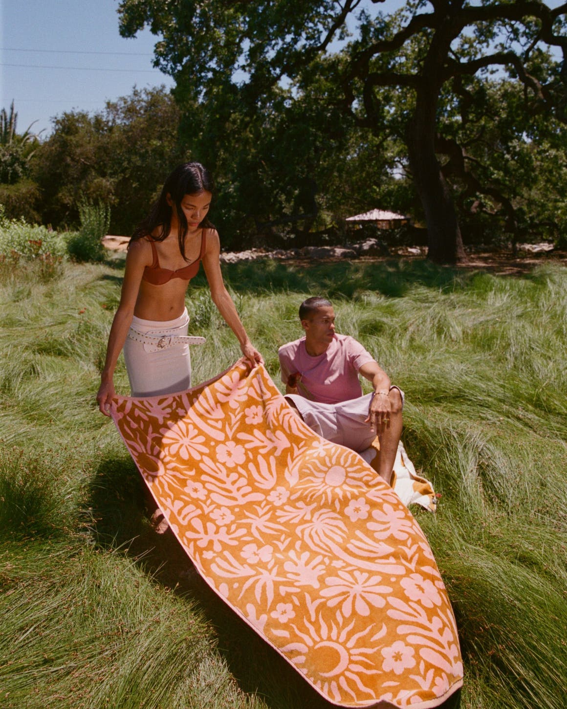 A woman spreading a patterned blanket on a grassy field.