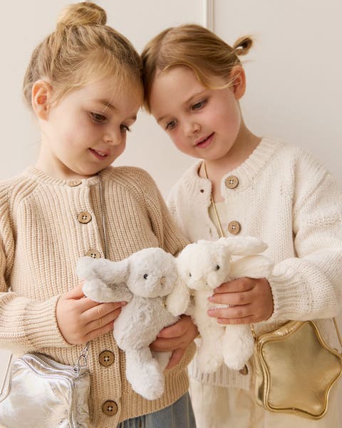 Two girls wearing cardigans and holding bunny stuffed animals.