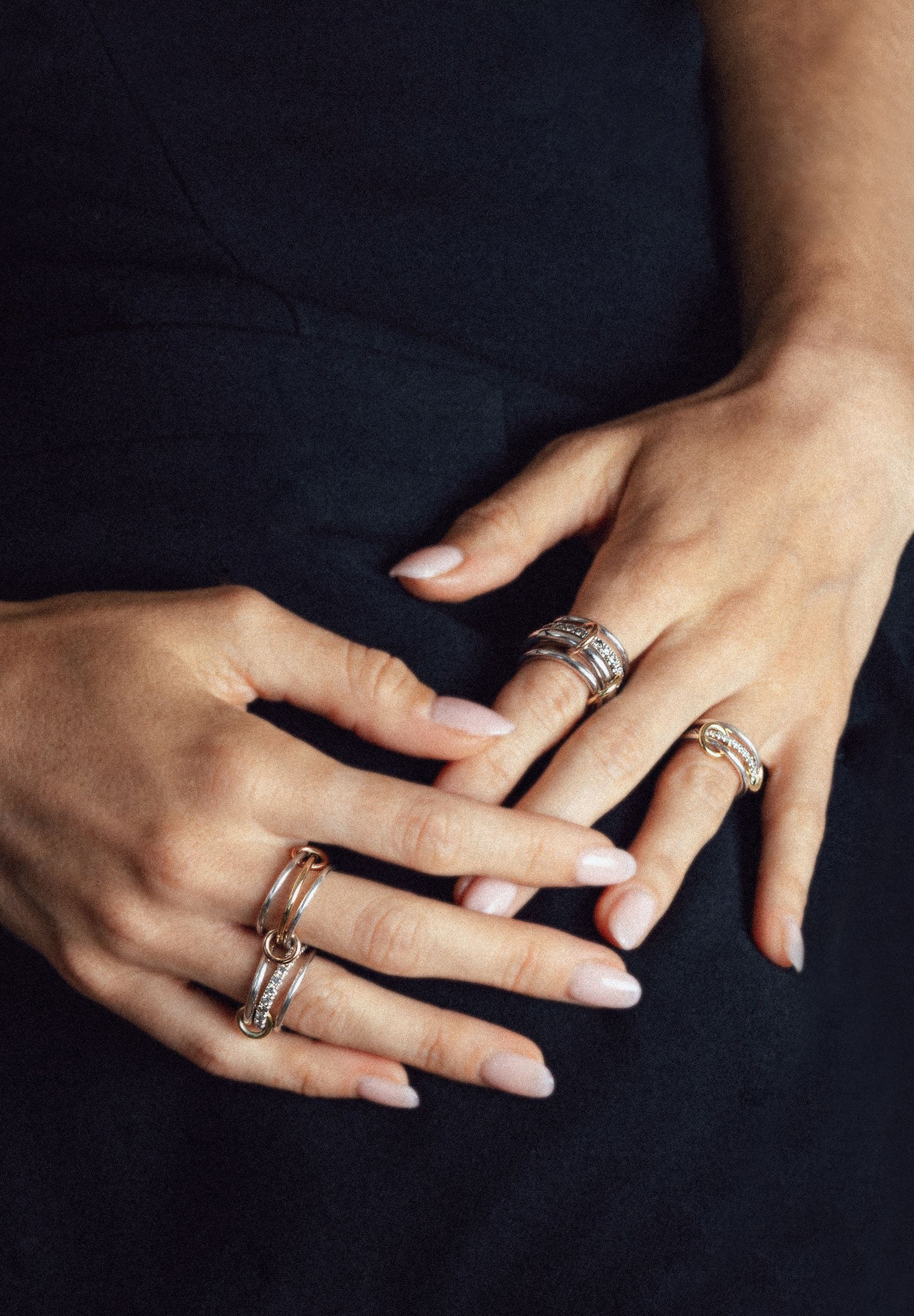 A pair of hands wearing multiple gold and silver-toned rings. 