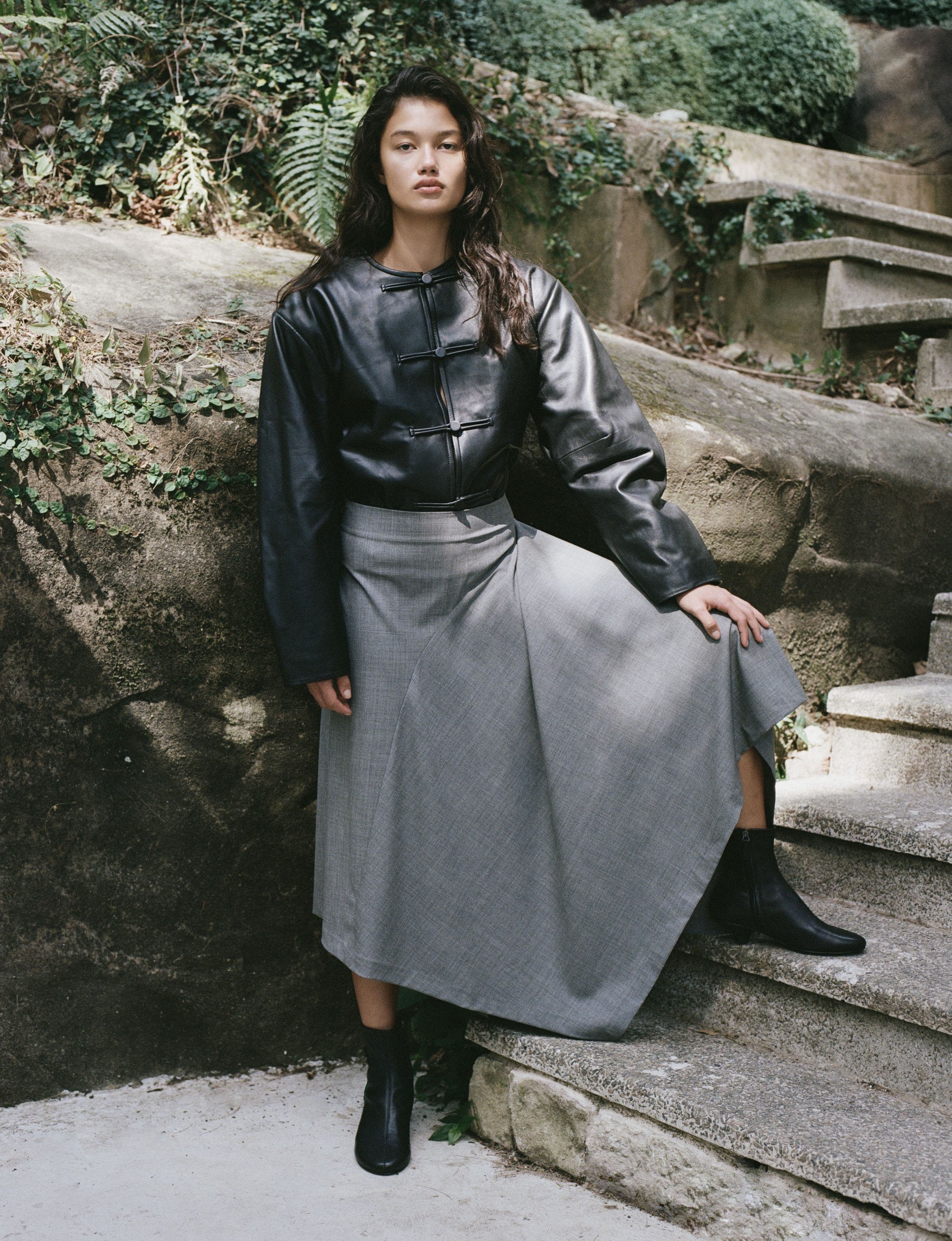 A woman wearing a black leather jacket and a grey maxi skirt.