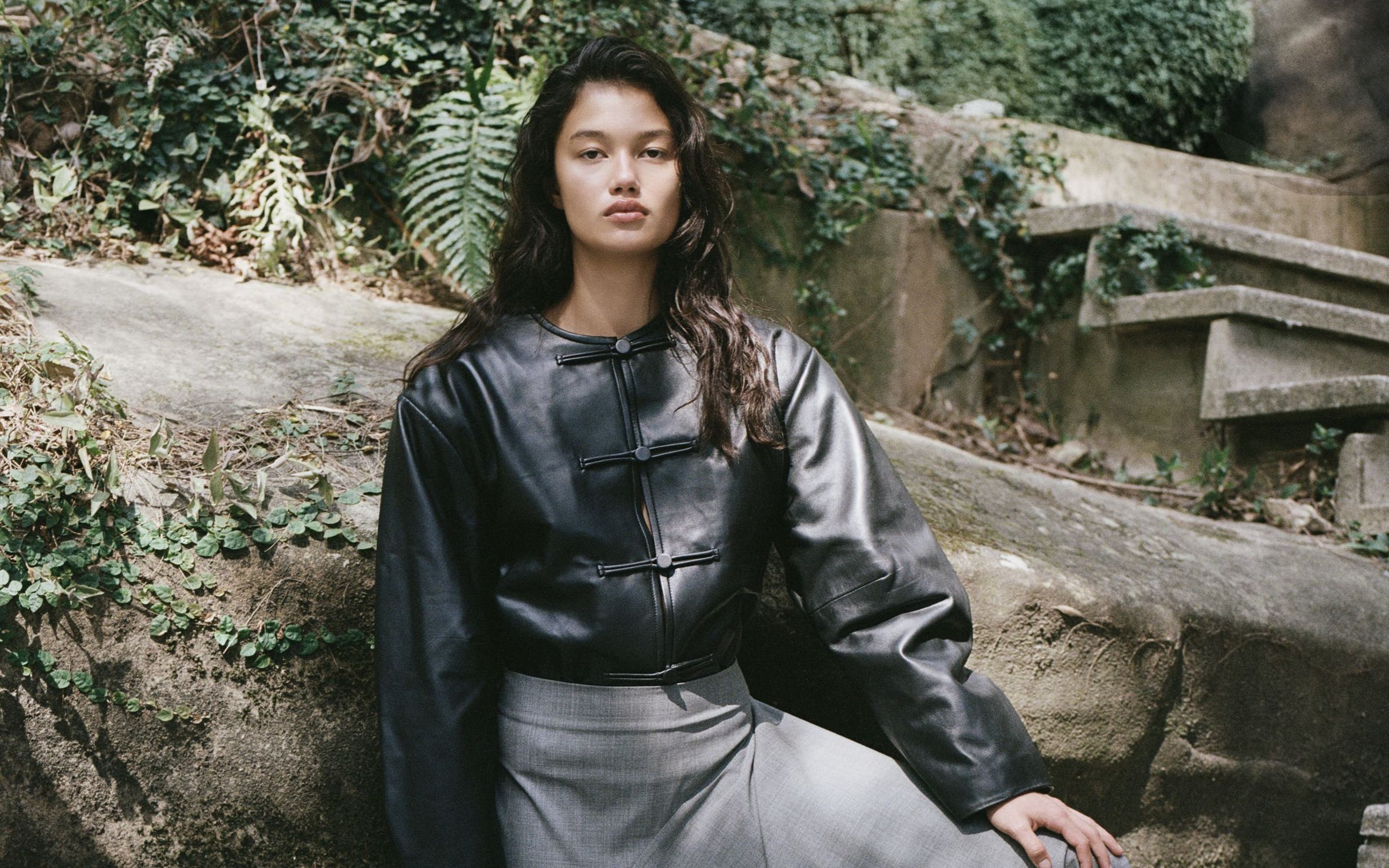 A woman wearing a black leather jacket and a grey maxi skirt.
