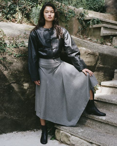 A woman wearing a cropped leather jacket, a grey wool maxi skirt, and black boots.
