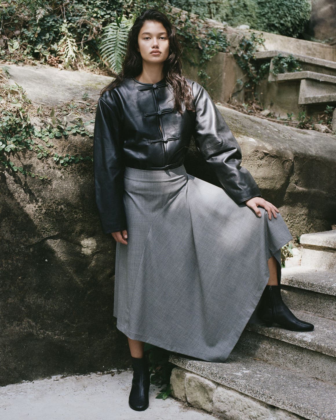 A woman wearing a black leather jacket and a grey maxi skirt.
