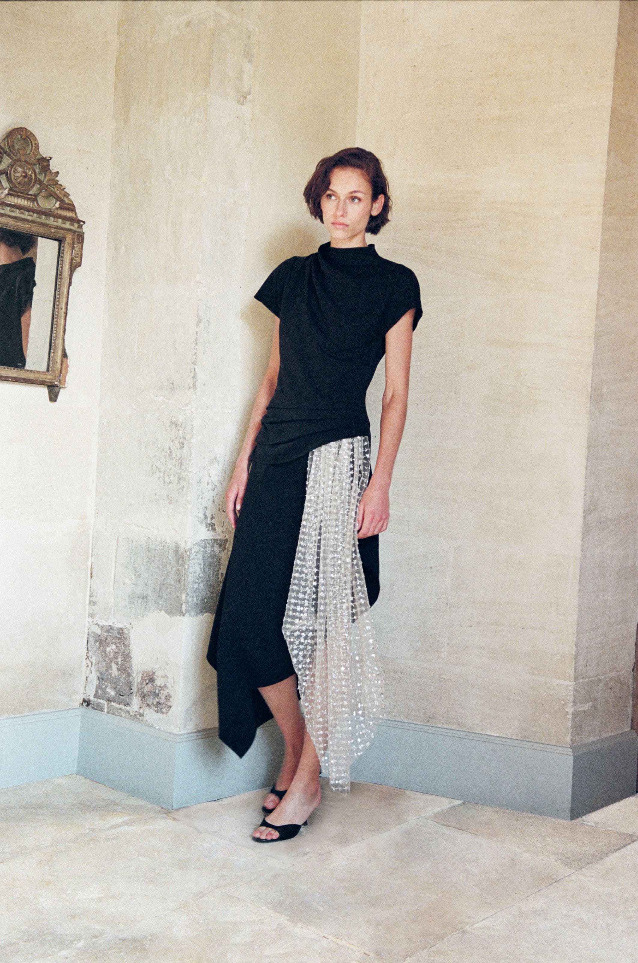 A woman wearing a black dress with a sheer lace skirt.
