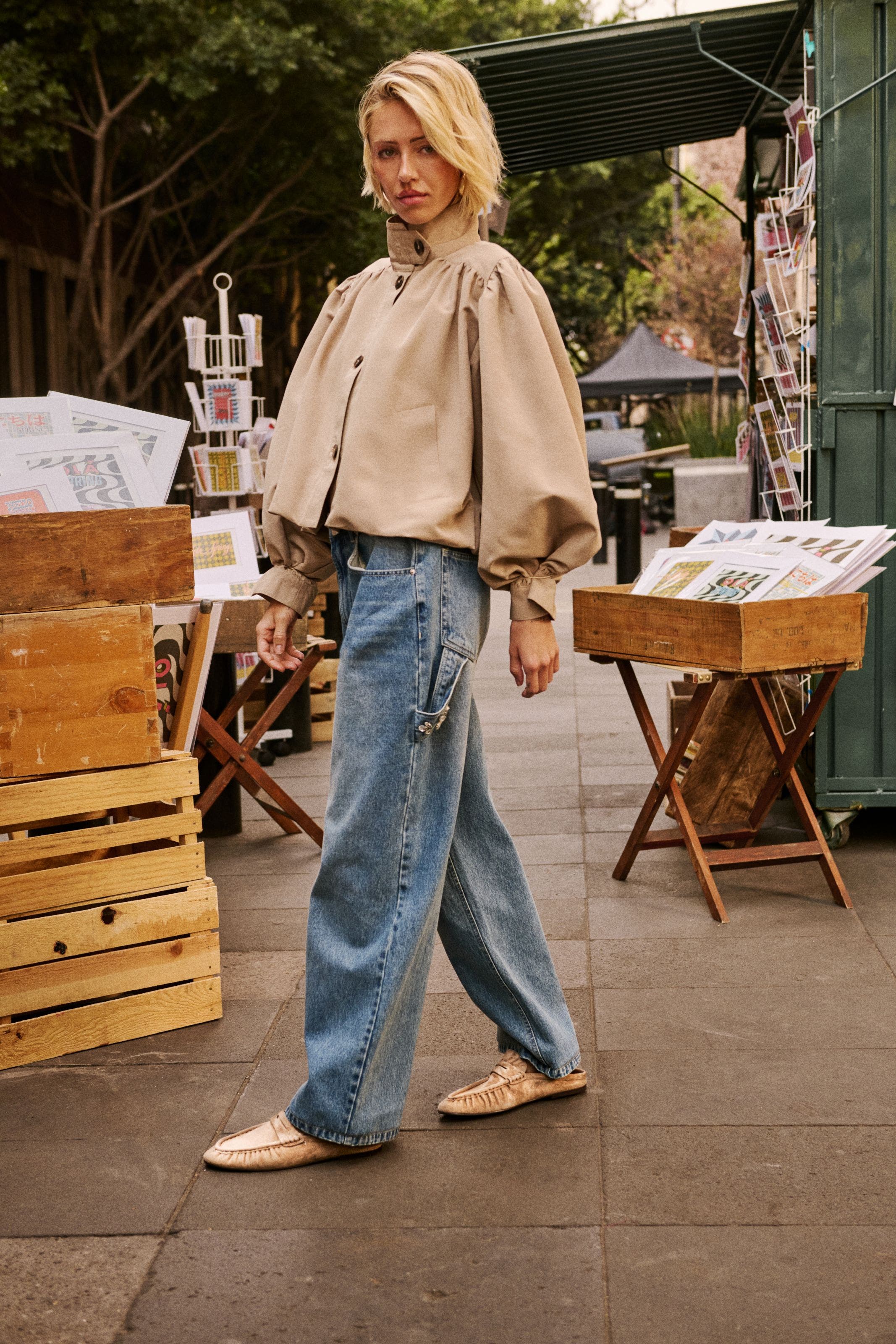 A woman in a cropped beige blouson-sleeved jacket and wide-leg jeans.
