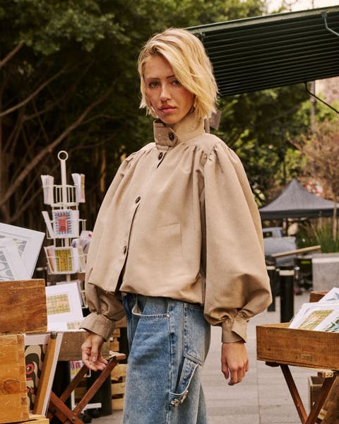 A woman in a cropped beige blouson-sleeved jacket and wide-leg jeans.