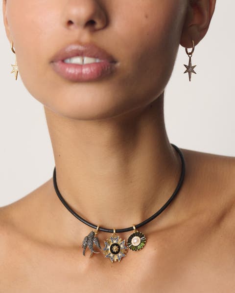 A woman wearing a necklace with several charms and pair of star shaped earrings. 