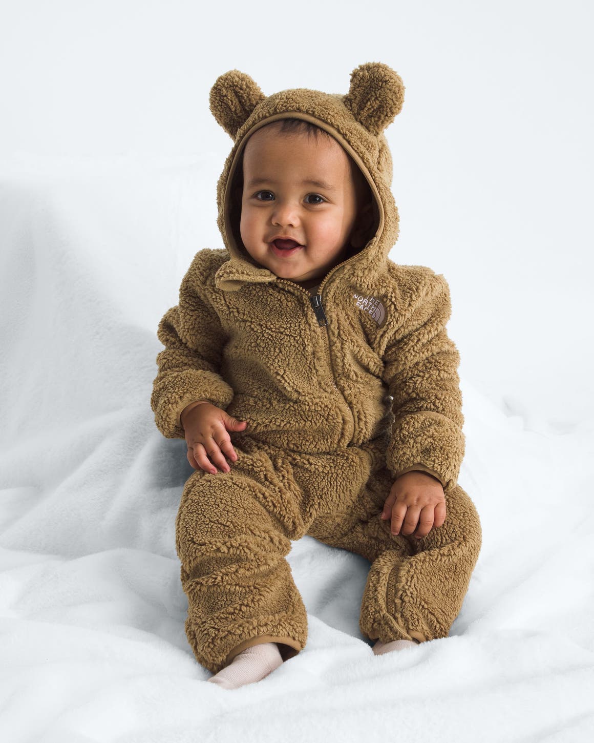 A baby in a brown teddy sherpa jumpsuit from The North Face.