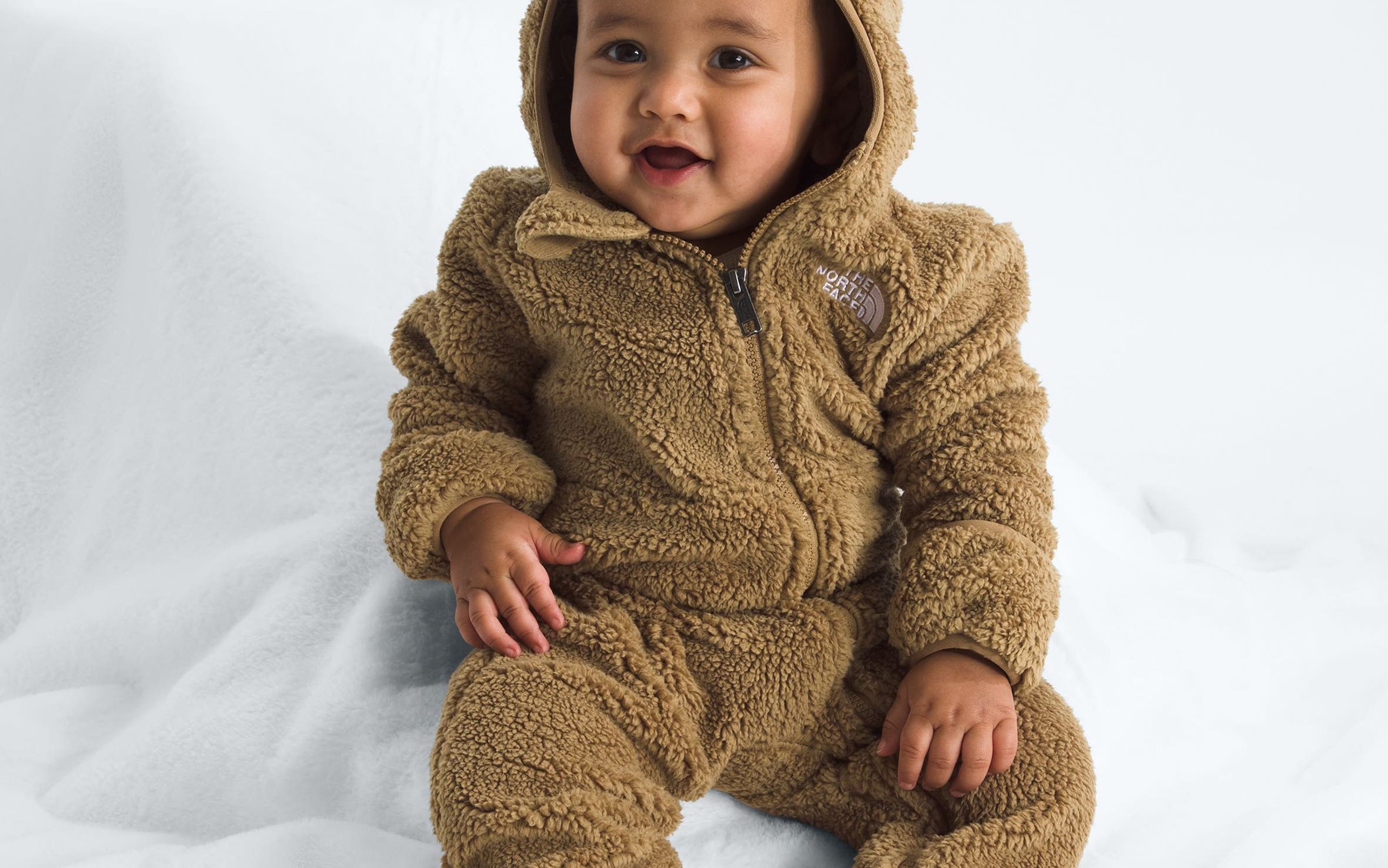 A baby in a brown teddy sherpa jumpsuit from The North Face.