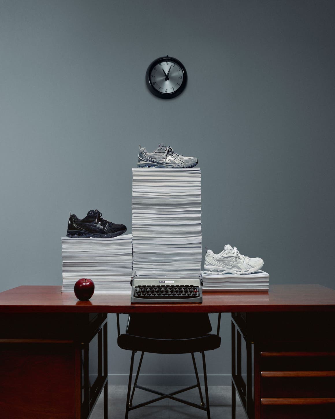 Thom Browne x ASICS sneakers on piles of paper on top of a desk. 