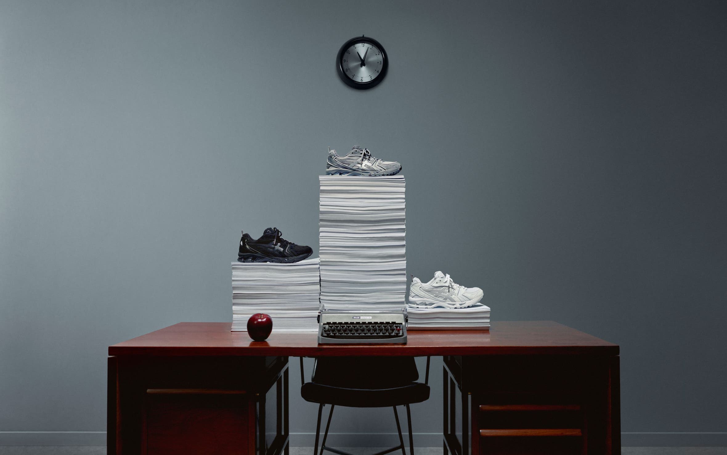 Thom Browne x ASICS sneakers on piles of paper on top of a desk. 