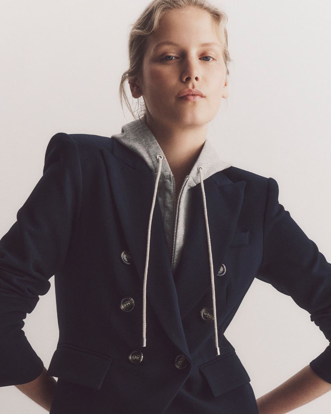Woman wearing a Veronica Beard navy blazar over a grey hoodie.
